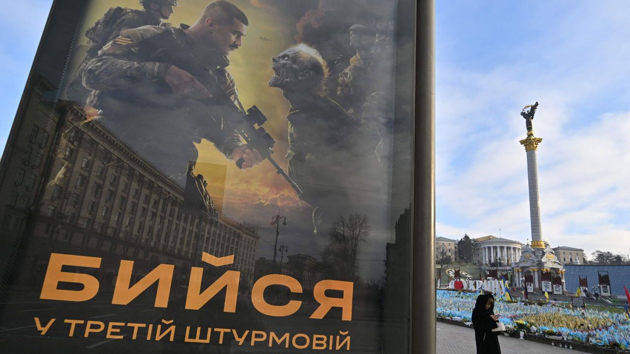 A woman walks past a poster depicting Ukrainian servicemen fighting with evils