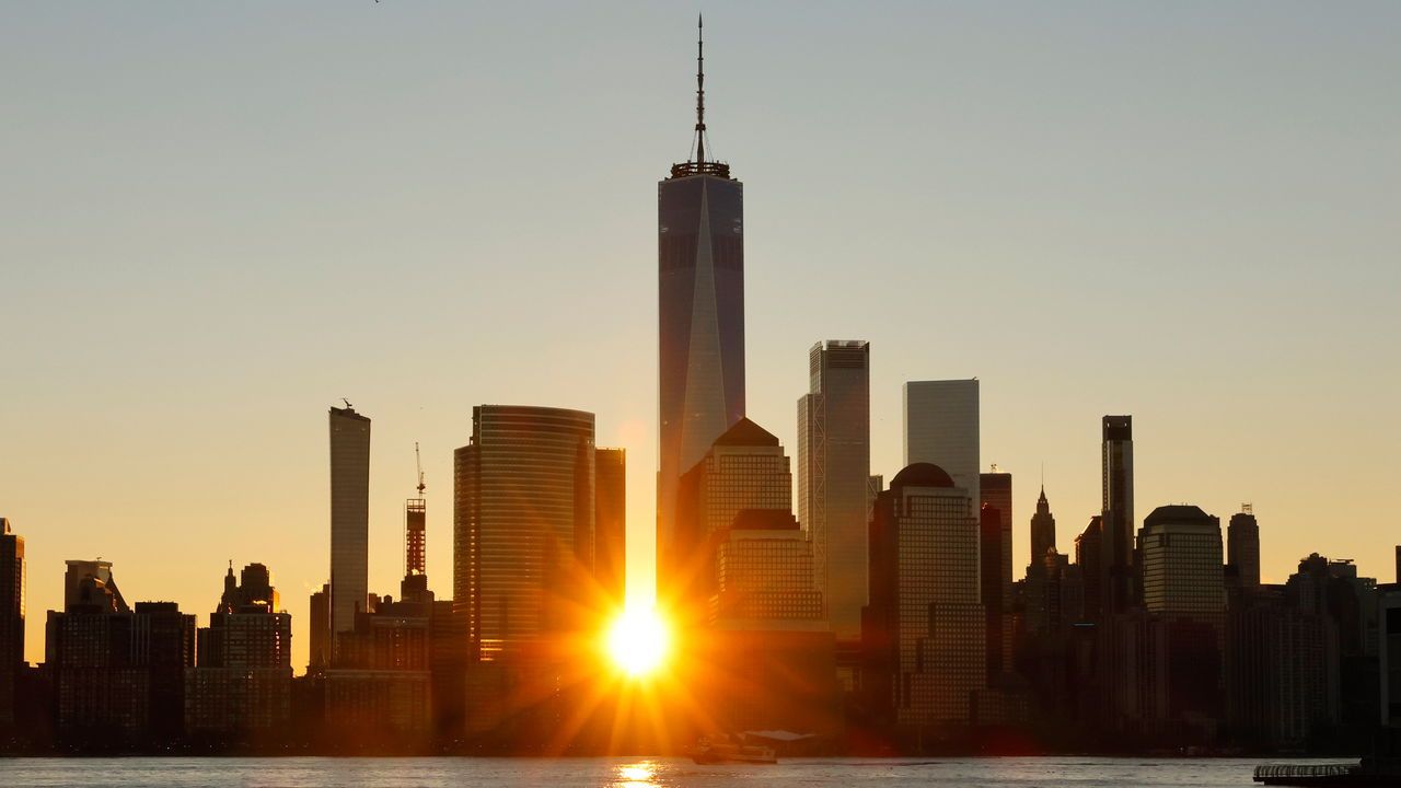 The sun rises behind the skyline of lower Manhattan and One World Trade Center in New York City.